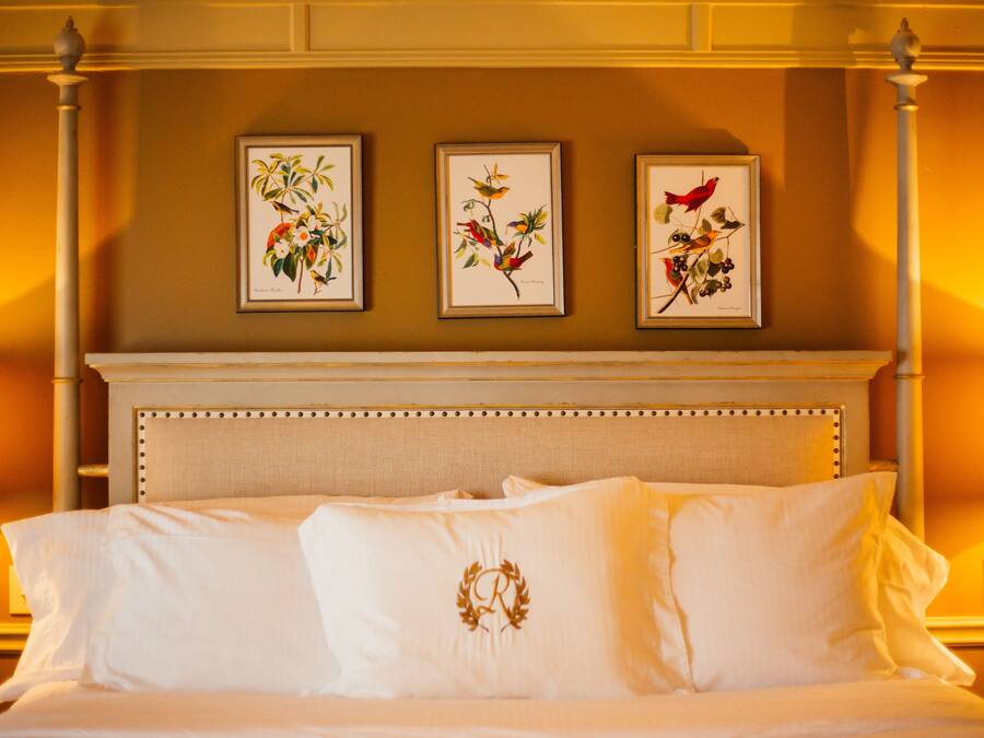 Une chambre d’hôtel avec un lit, une tête de lit et trois reproductions encadrées de motifs botaniques accrochées au mur.