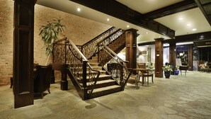 Een ruime lobby met een stenen vloer, een statige trap met versierde balustrades, en een grote potplant.