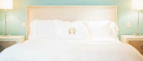 A neatly made bed with white linens and a decorative pillow, flanked by two bedside tables with lamps, set against a teal wall.