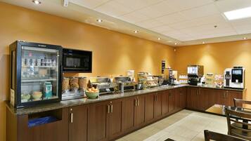 A hotel kitchen with a self-service breakfast bar, a refrigerator, microwave, and various food items.