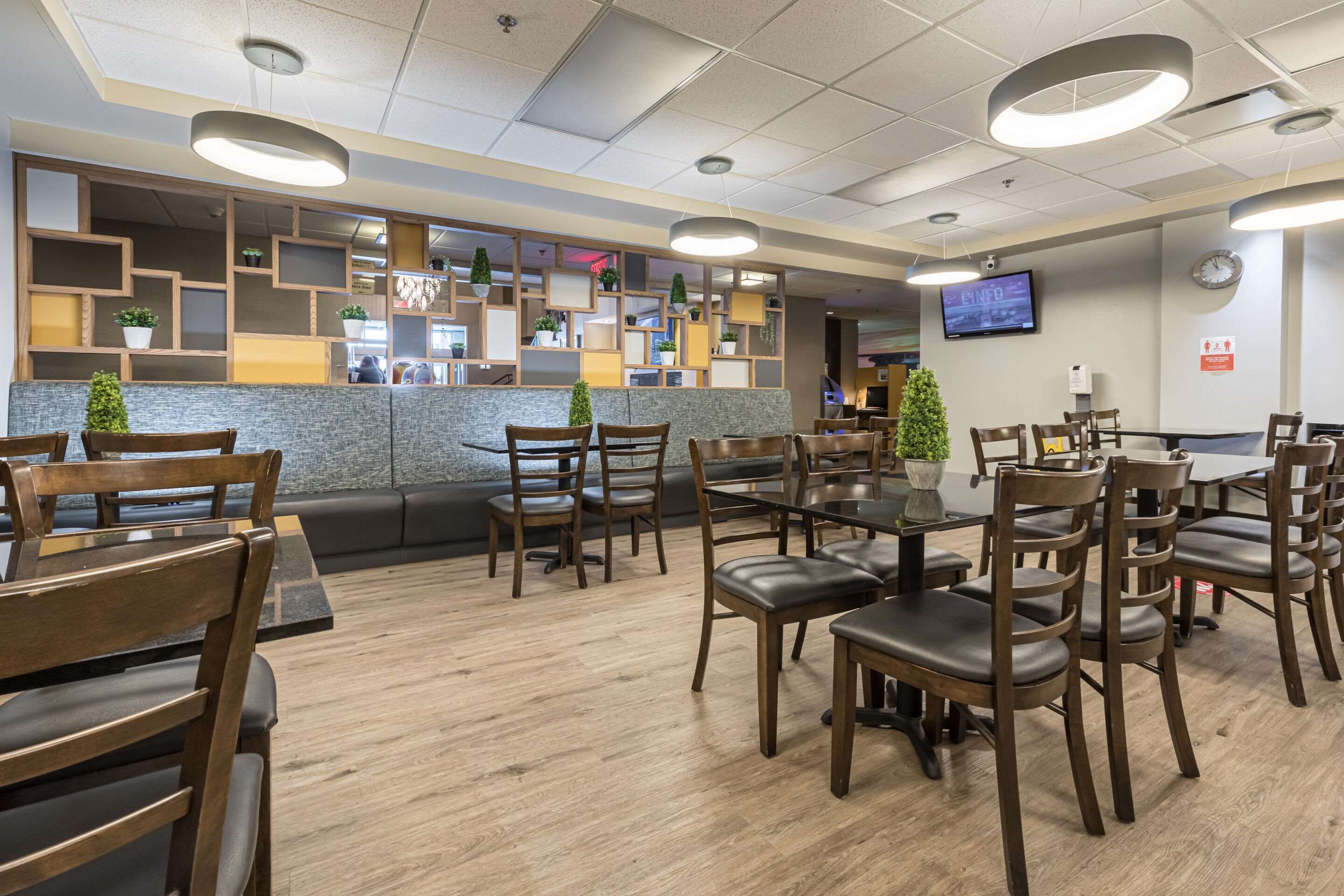 A modern restaurant with wooden furniture, a counter with plants, and a TV on the wall.