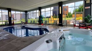 A large indoor pool area with multiple hot tubs and seating areas, surrounded by large windows offering views of the outside.