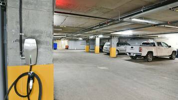 A parking garage with concrete pillars, electric vehicle charging stations, and parked vehicles.