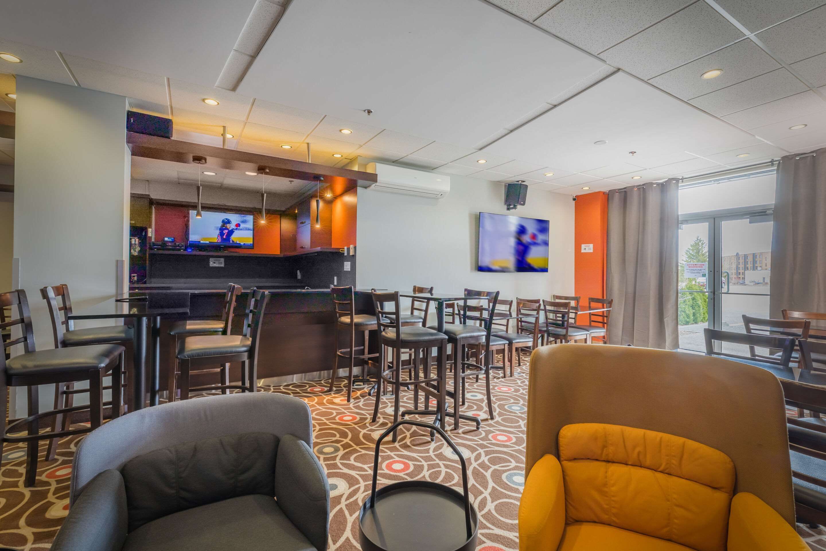 A hotel lobby with a bar area, multiple seating arrangements, and a television mounted on the wall.