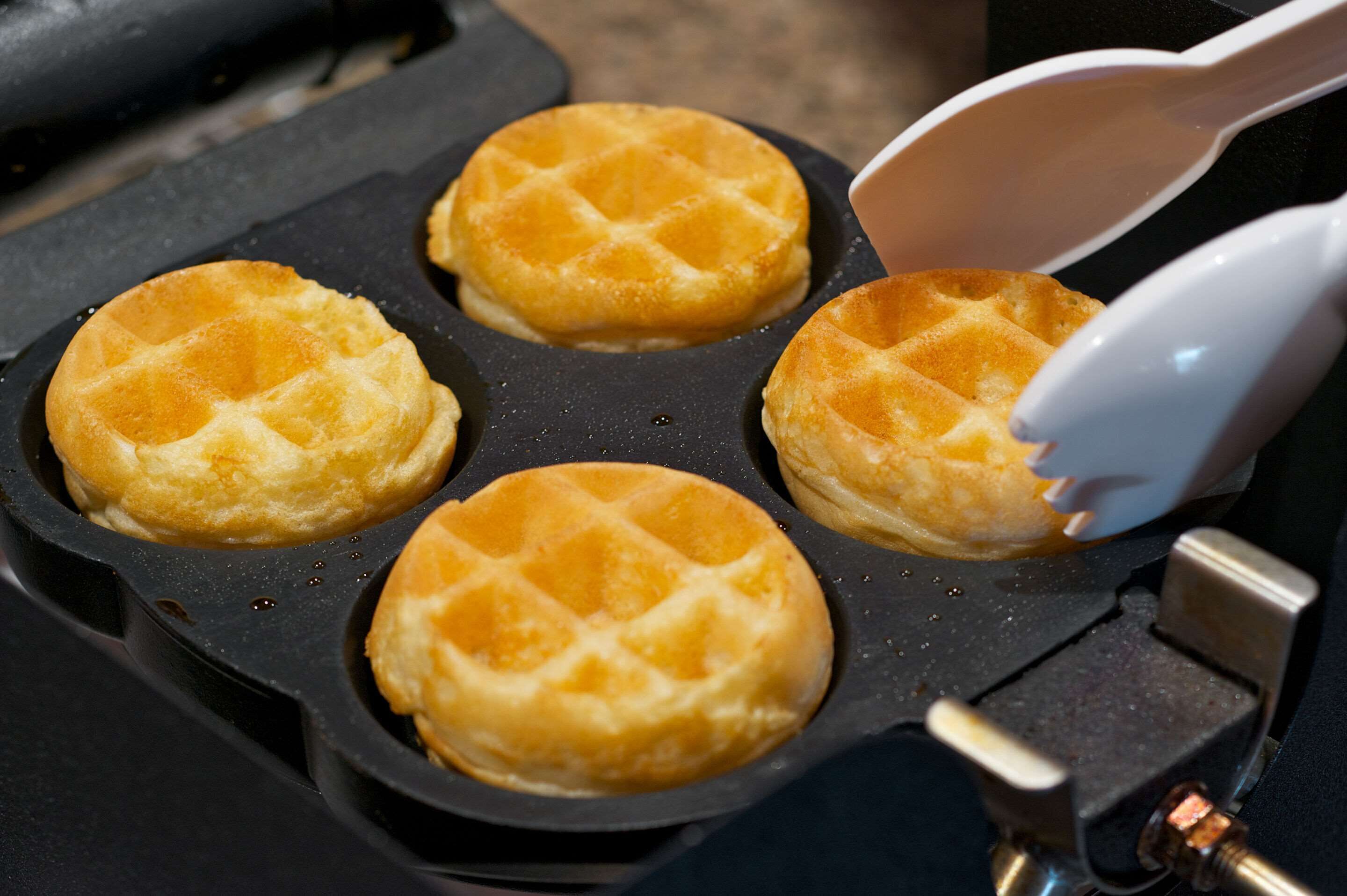 Una piastra per waffle con quattro waffle che vengono rimossi con una spatola bianca.