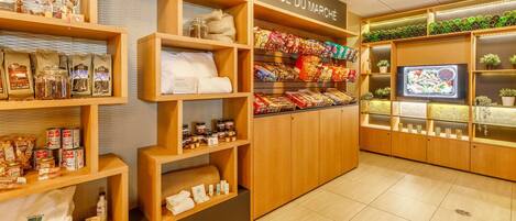 Una tienda bien organizada con estantes llenos de diversos productos alimenticios y un televisor mostrando un plato de comida.