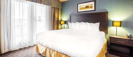 A hotel room with a large bed, a nightstand with a lamp, and a framed picture on the wall.