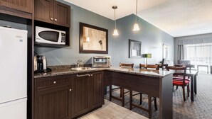 A modern kitchen with dark wood cabinets, a built-in microwave, a toaster, and a granite countertop. There is a dining area with a table and chairs, and a large window providing natural light.