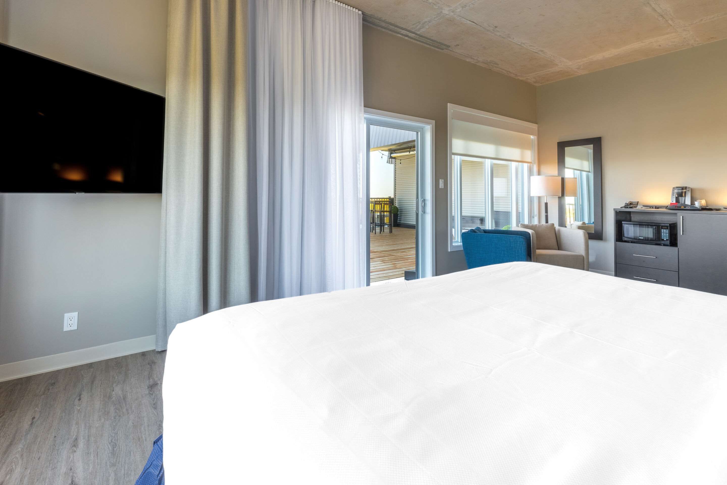 A hotel room with a large bed, a desk with a lamp, a microwave, and a view of the outdoor area.