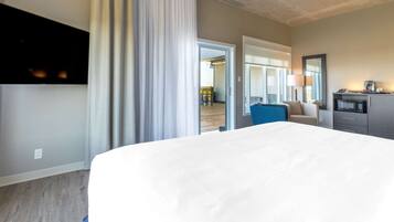 A hotel room with a large bed, a desk with a lamp, a microwave, and a view of the outdoor area.