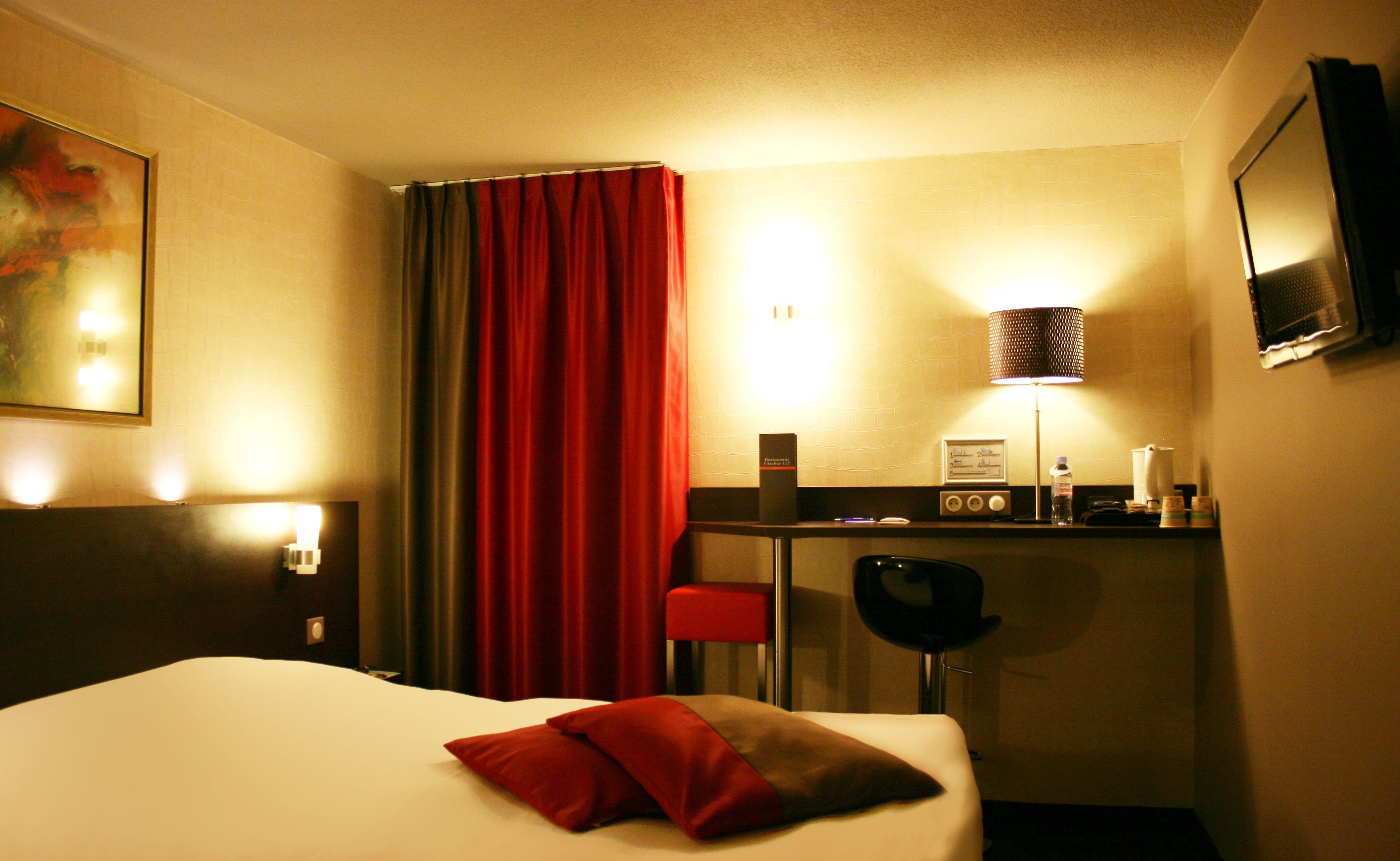 Een hotelkamer met een bed, een bureau met stoel, een televisie en een lamp.