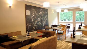 Un restaurant au décor moderne, avec un grand tableau abstrait accroché au mur, de nombreuses tables et chaises, et une vue sur la verdure par les fenêtres.