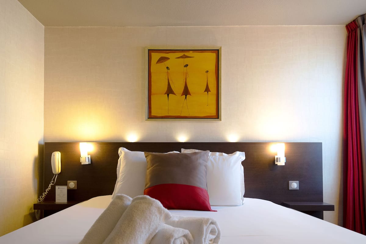 Une chambre d’hôtel avec un lit bien fait, une table de chevet avec un téléphone et une lampe, et un tableau accroché au mur.