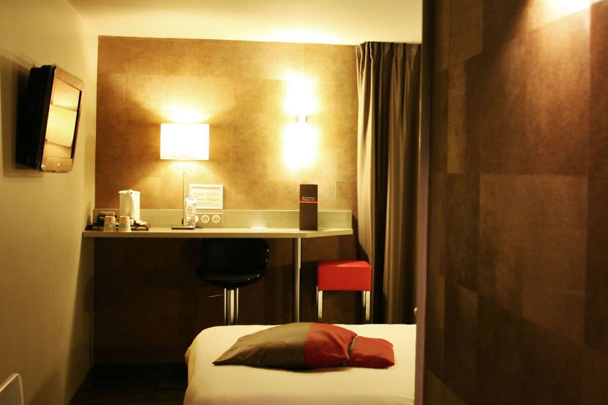 Une chambre d’hôtel équipée d’un lit, d’un bureau, d’une chaise, d’une lampe et d’un téléviseur fixé au mur.