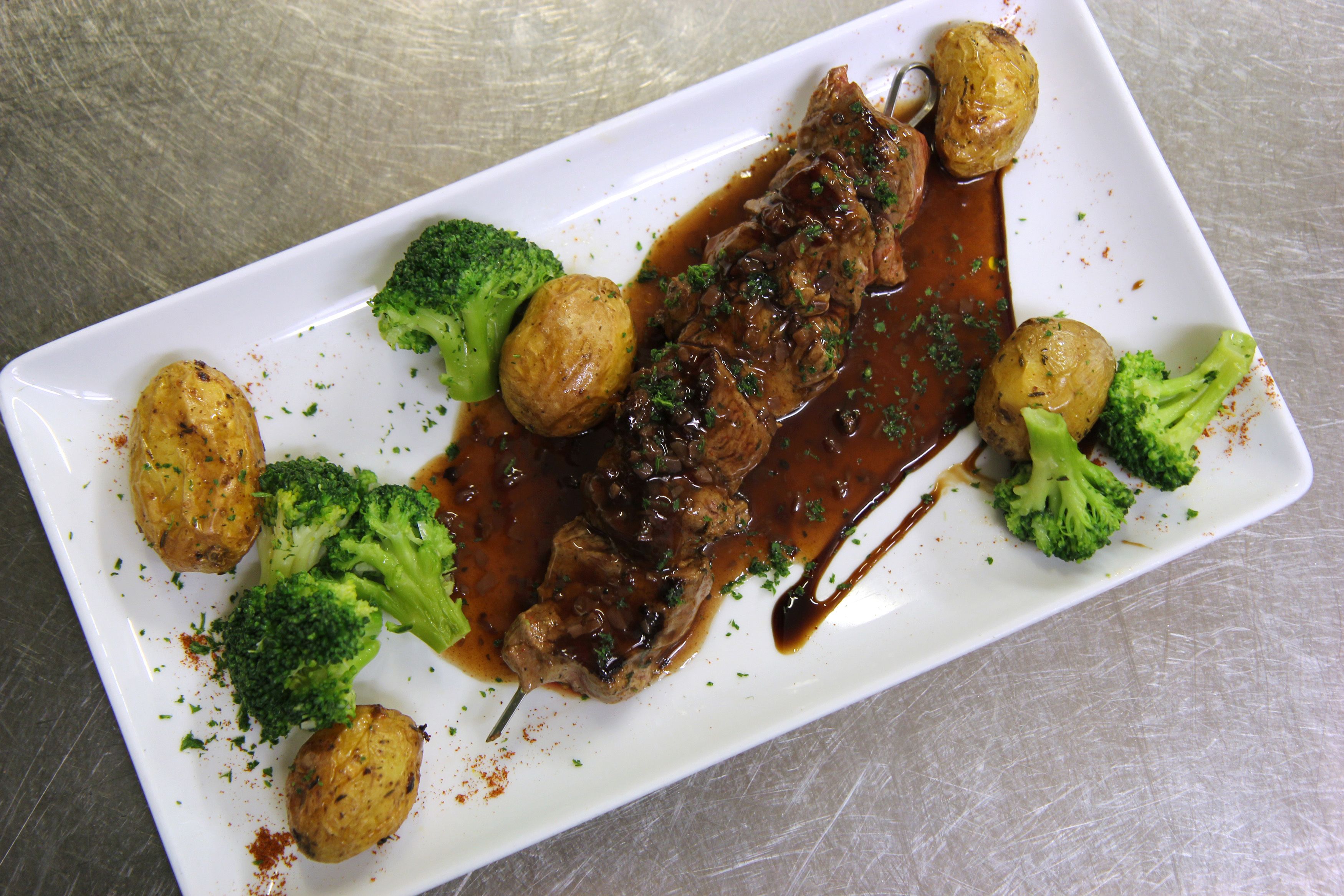 A rectangular white plate with a beef dish, broccoli, and potatoes.