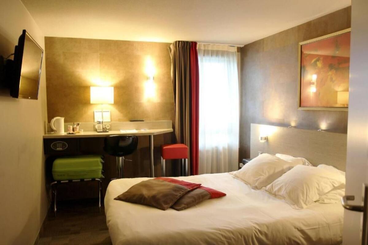 Une chambre d’hôtel avec un lit, un bureau et une chaise, une télévision et un tableau au mur.