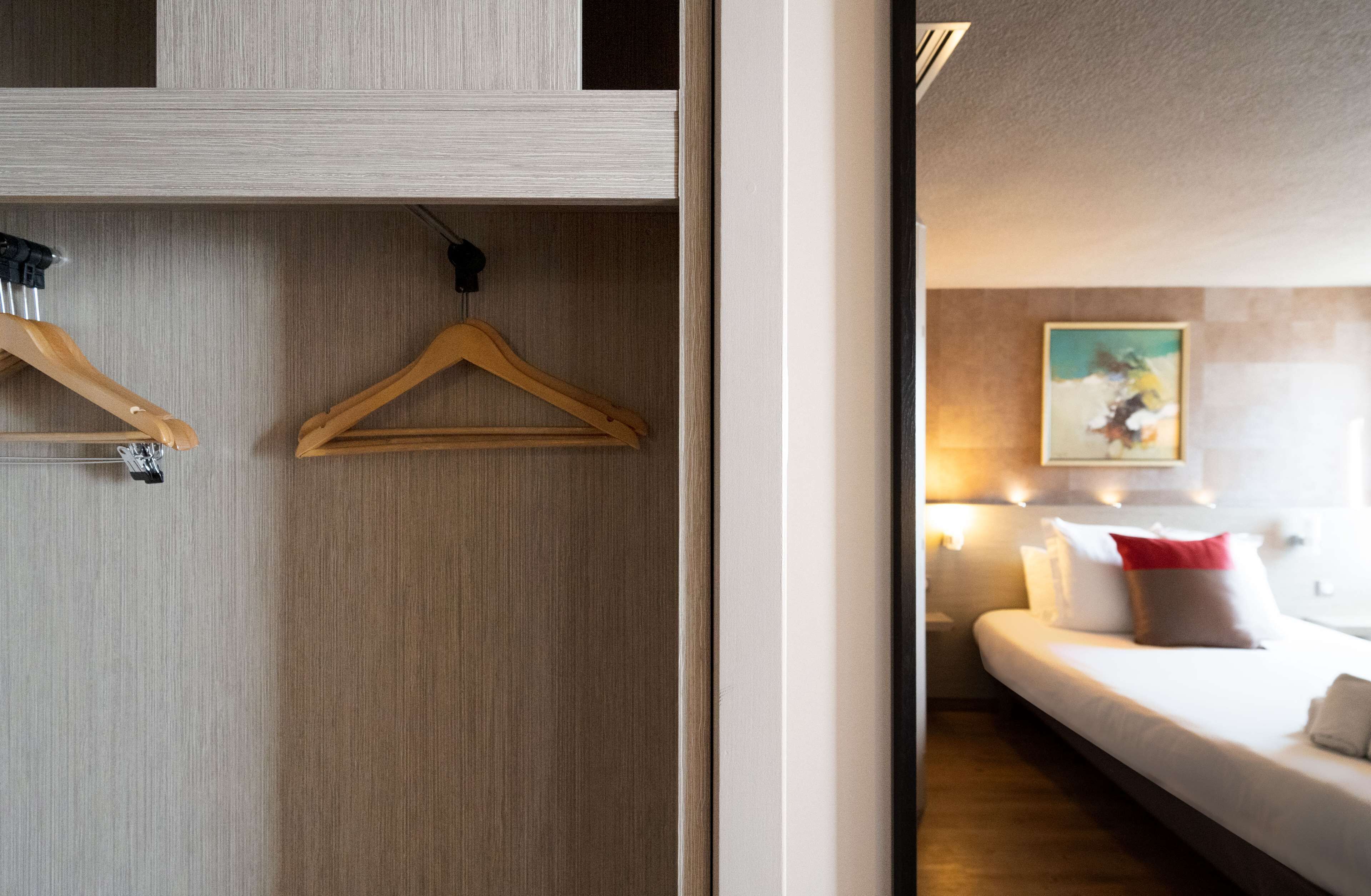Et hotelværelse med et træskab, en seng med hvide sengetæpper og en rød pude, samt et maleri på væggen.