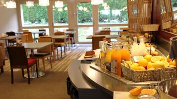 Een ontbijtbuffet met tafels, stoelen en diverse ontbijtartikelen, zoals fruit en sap.