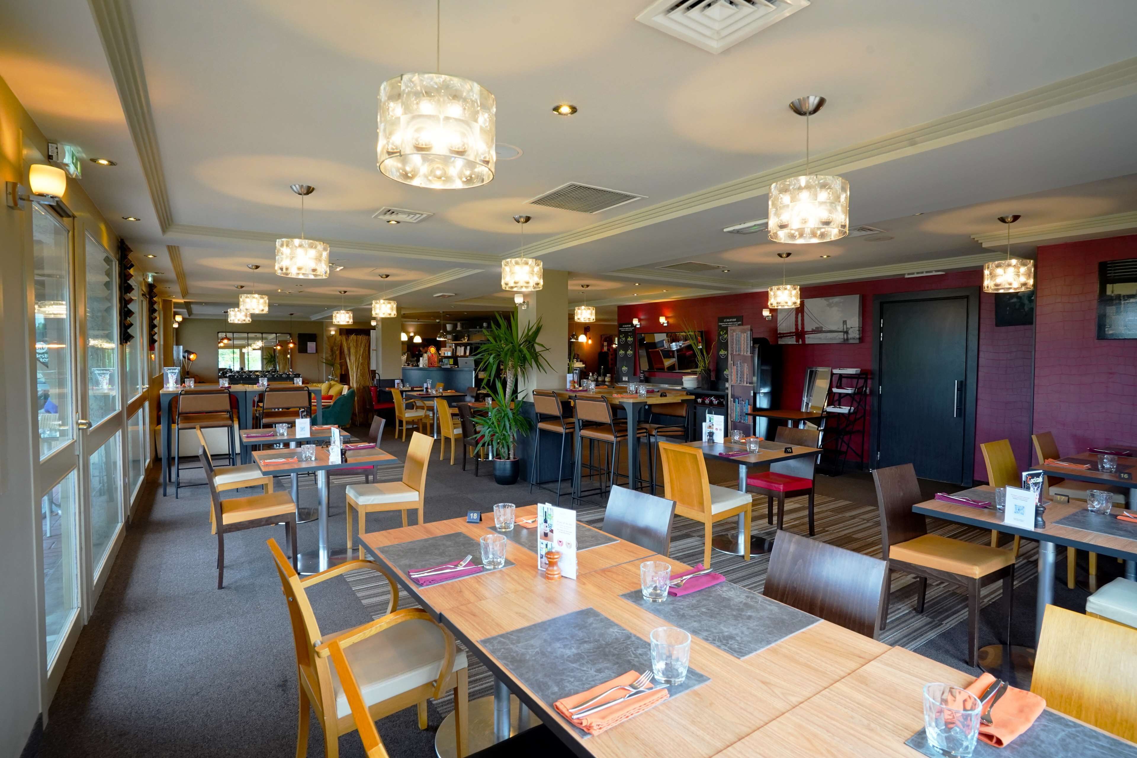 Ein geräumiges Restaurant mit mehreren Tischen und Stühlen, großen Fenstern und hängenden Pendelleuchten.