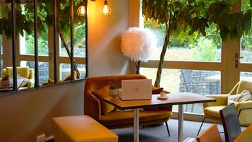 A modern interior with a laptop on a table, a sofa, and a large window with a view of greenery.