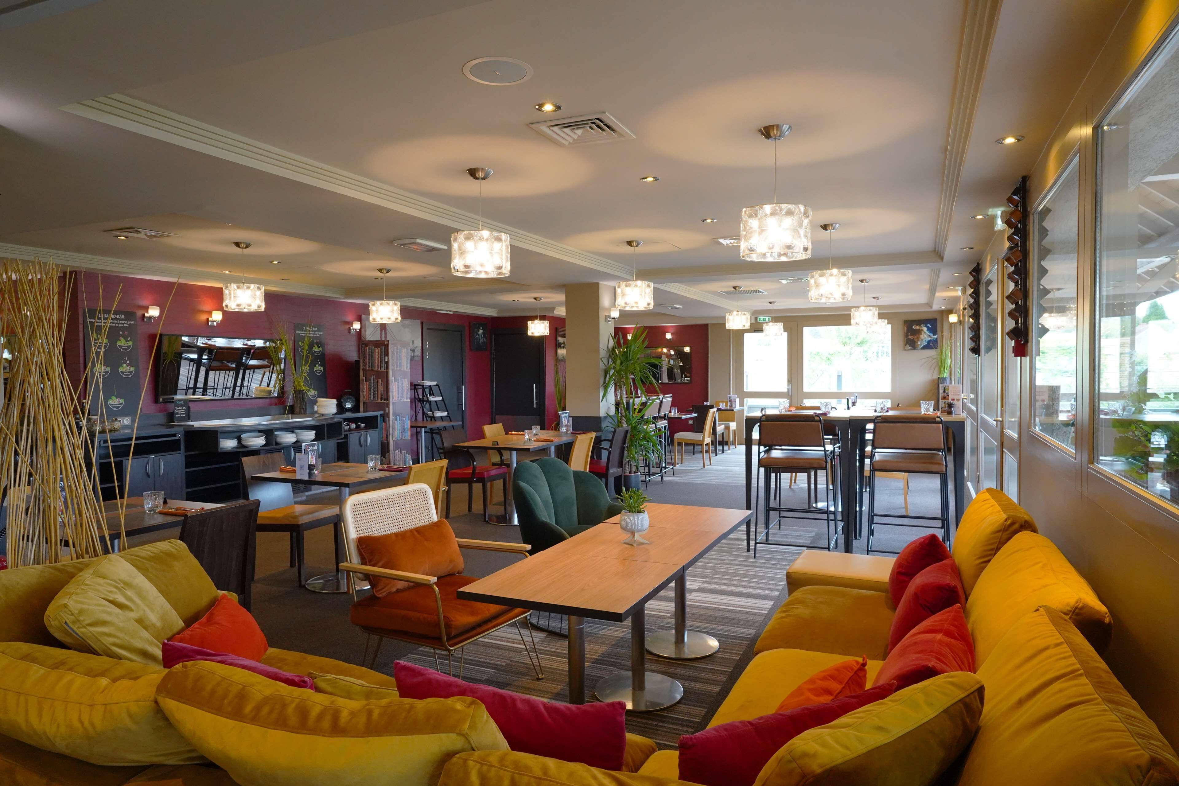 A modern hotel lobby with vibrant yellow sofas, a wooden coffee table, and a mix of dining and seating areas.