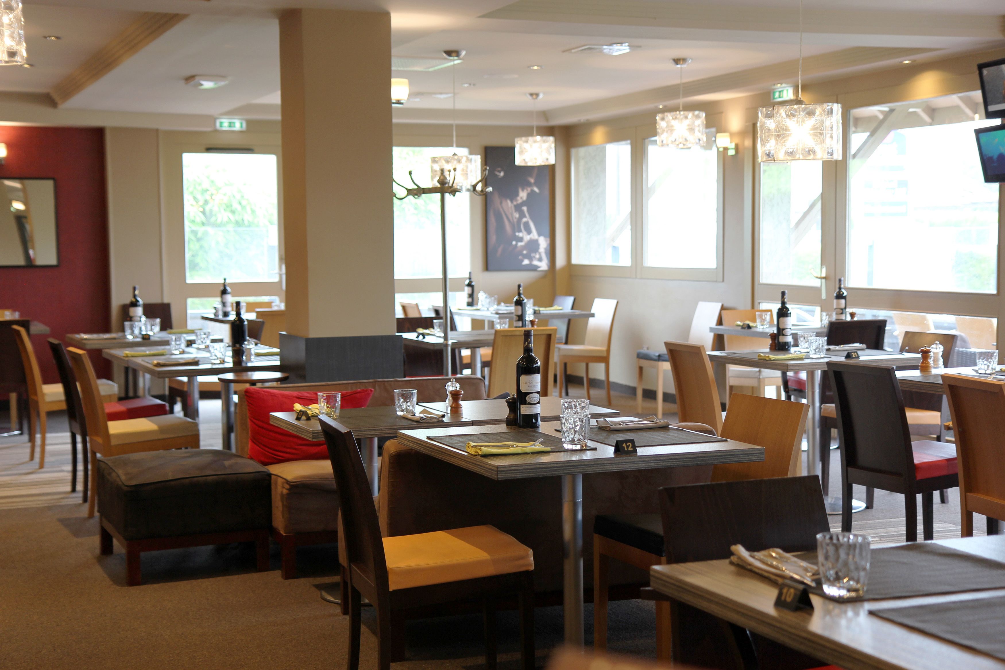 Un restaurante con varias mesas y sillas, ventanas amplias y candelabros colgantes.
