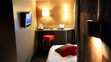 A hotel room with a bed, a desk with a laptop, a TV, and a red stool.
