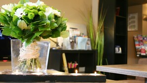 A clear glass vase with white flowers and green leaves on a table, with candles and a black shelf in the background. - Best Western l'Atelier 117 (Maubeuge)