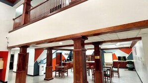 A spacious lobby with a high ceiling, a wooden balcony, and a modern kitchen area in the background.