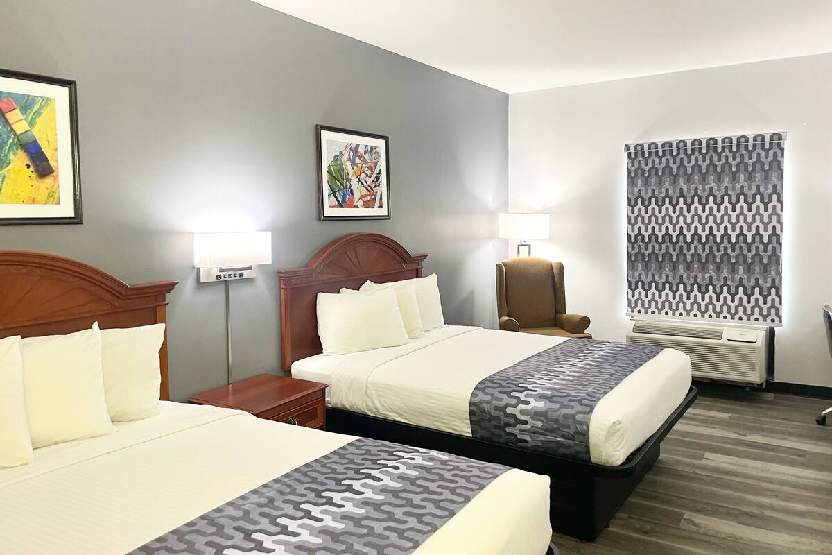 Une chambre d’hôtel avec deux lits, une chaise, un bureau et une fenêtre avec des rideaux à motifs.