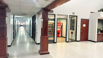 A long, narrow hallway with wooden pillars, glass doors, and a vending machine.