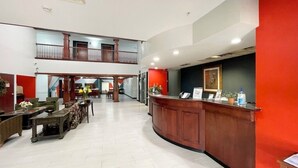 A hotel lobby with a reception desk, seating area, and a staircase leading to an upper level.