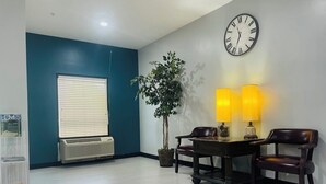 A room with a dark blue accent wall, a white air conditioning unit, a table with two chairs, a potted plant, and a wall clock.