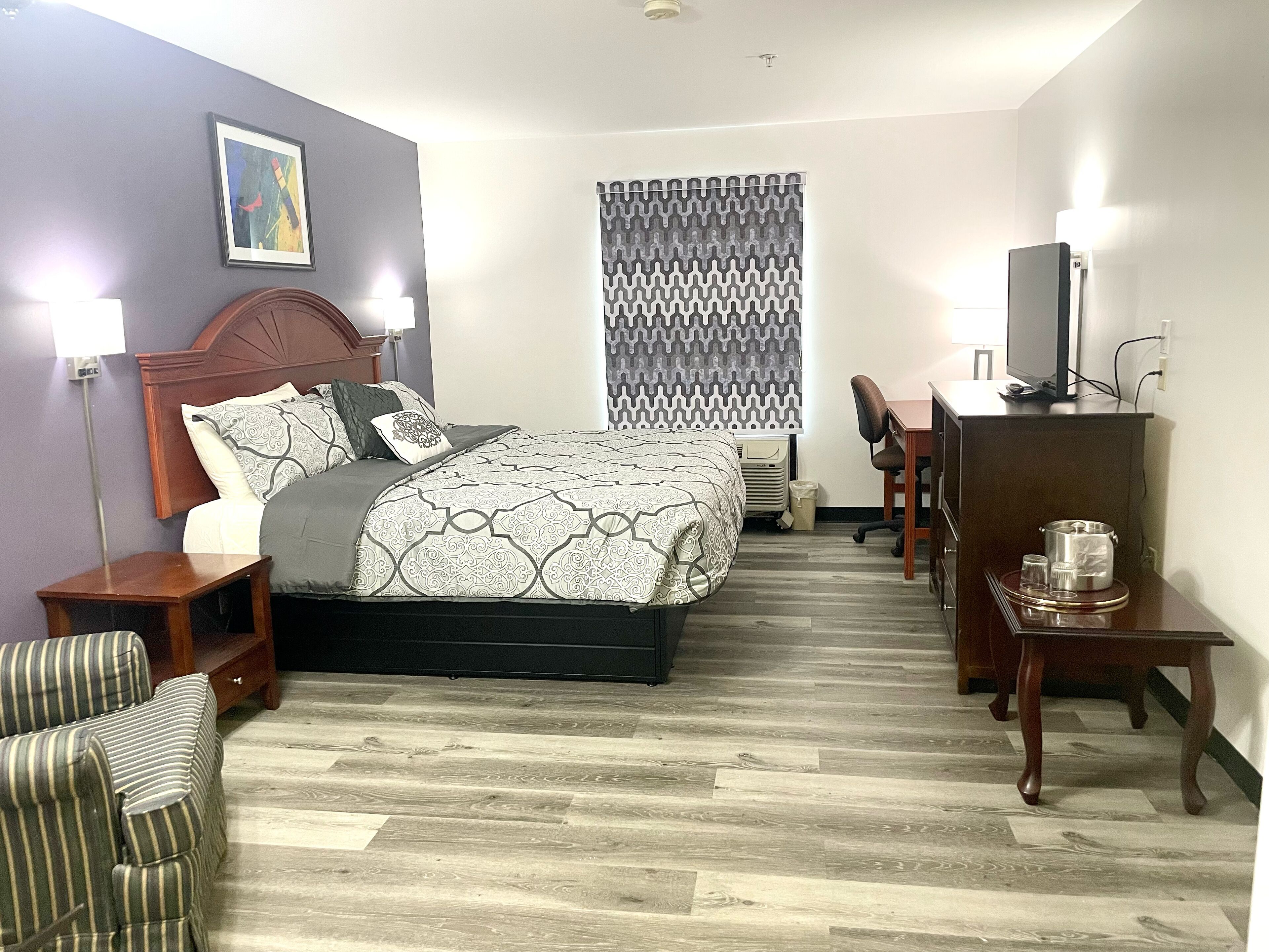A hotel room with a bed, a desk, a chair, a television, and a window with patterned curtains.