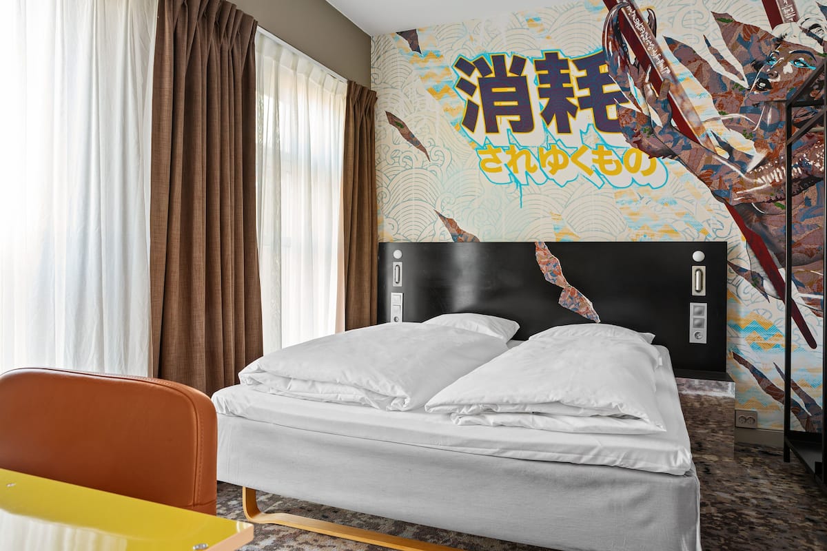 Una camera d'albergo con un letto, una sedia, un tavolo e un muro decorato da un murale colorato.