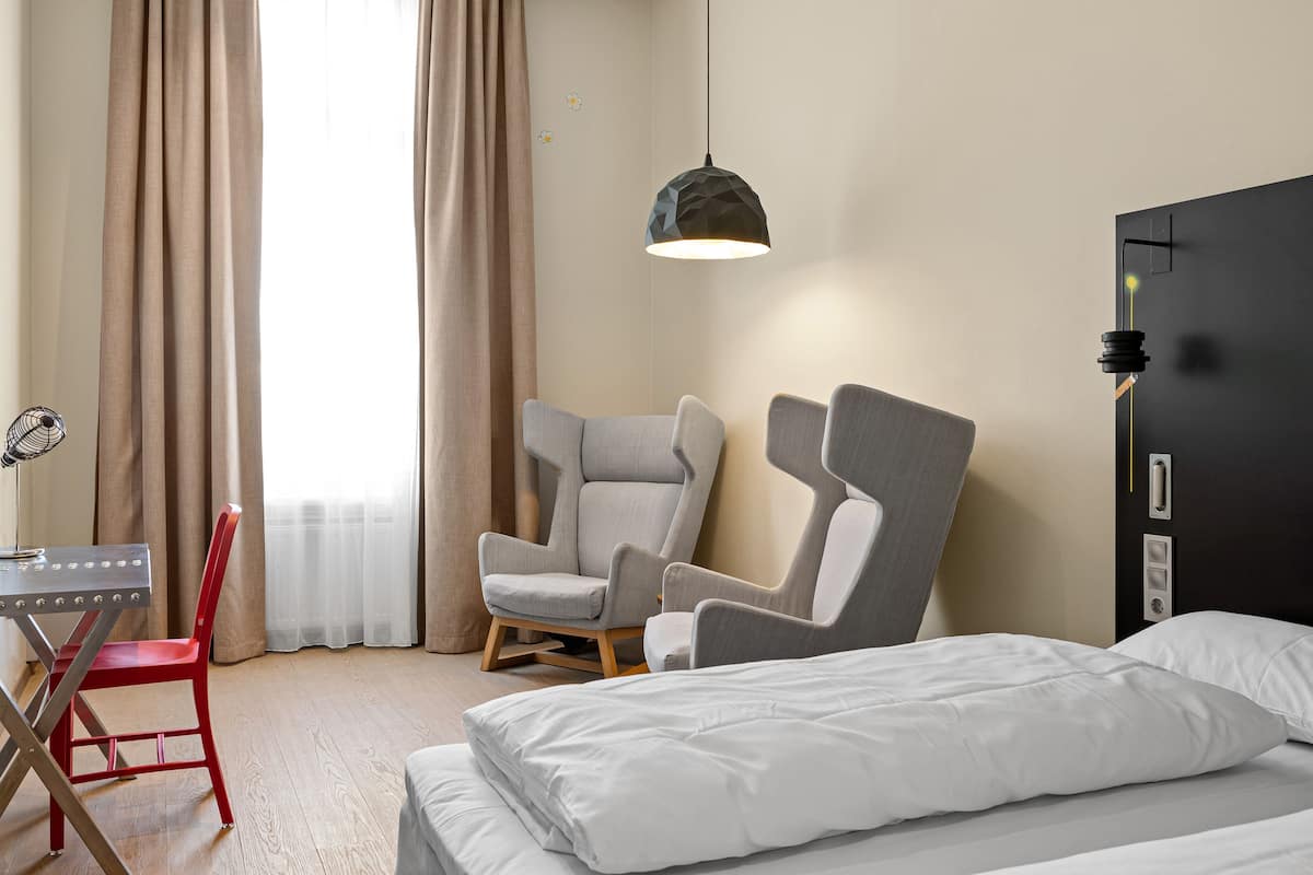 Una camera d'albergo con un letto, due poltrone, una scrivania e una lampada.