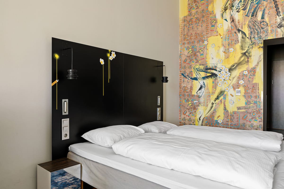 Una camera d'albergo con un letto grande, un comodino, una lampada a parete e un arazzo decorativo.