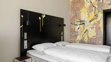 A hotel room with a large bed, a nightstand, a wall-mounted lamp, and a decorative tapestry.