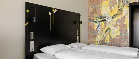 A hotel room with a large bed, a nightstand, a wall-mounted lamp, and a decorative tapestry.