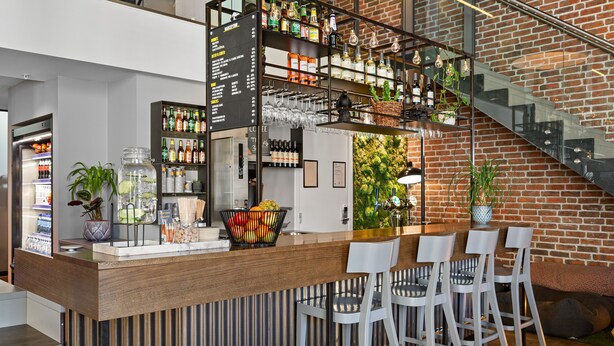 A modern bar area with a wooden counter, bar stools, and a menu board. - Comfort Hotel Grand Central (Oslo)