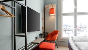 A modern hotel room with a bed, a desk, a chair, a TV, and a window with a city view. - Comfort Hotel Grand Central (Oslo)