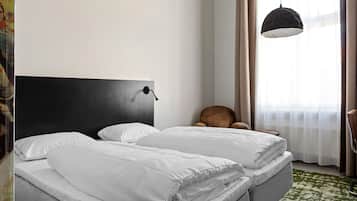 A hotel room with a bed, a headboard, a hanging light fixture, a chair, and a window with curtains.