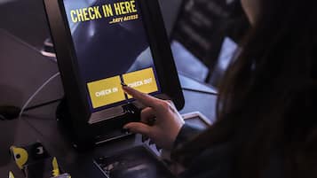 Una persona utilizando un quiosco de autoservicio con opciones para registrarse o salir.