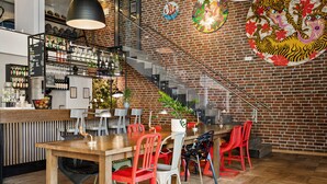 A restaurant with a wooden table, red and white chairs, a bar area with shelves of bottles, and a brick wall with decorative plates. - Comfort Hotel Grand Central (Oslo)