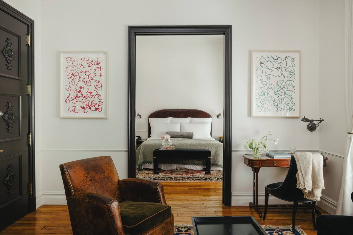 A bedroom with a bed, a chair, a table, and artwork on the walls.