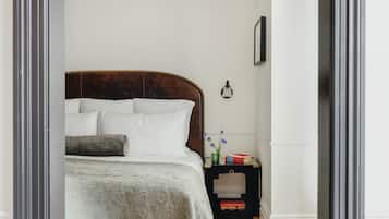 A neatly made bed with a wooden headboard, a bedside table with books and a vase of flowers, and a wall-mounted lamp.
