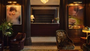 A lobby with a reception desk, a chandelier, leather chairs, and a patterned rug. - The Ned NoMad (New York)