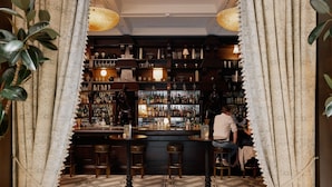 A bar area with a patterned floor, shelves with bottles, and stools. - The Ned NoMad (New York)