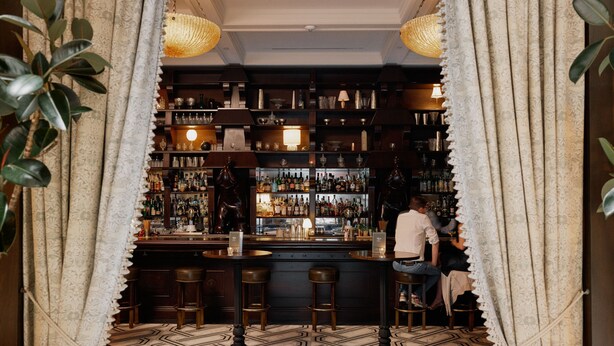 A bar area with a patterned floor, shelves with bottles, and stools. - The Ned NoMad (New York)
