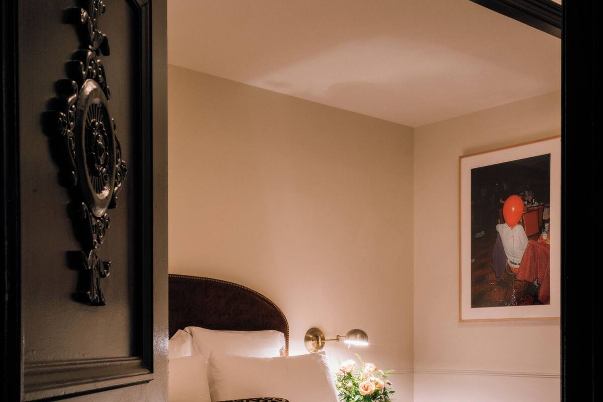 A bedroom with a bed, a bench, a bedside table with a lamp, and a floral arrangement.